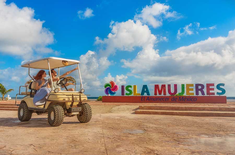 isla mujeres letters and a couple on a  golf cart