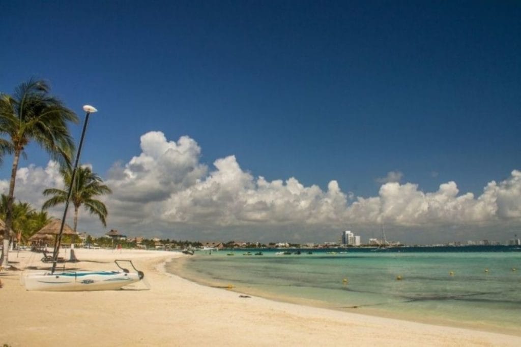 Cancun beach with clouds in the sky and a kayak on the beach - Cancun vs Tulum