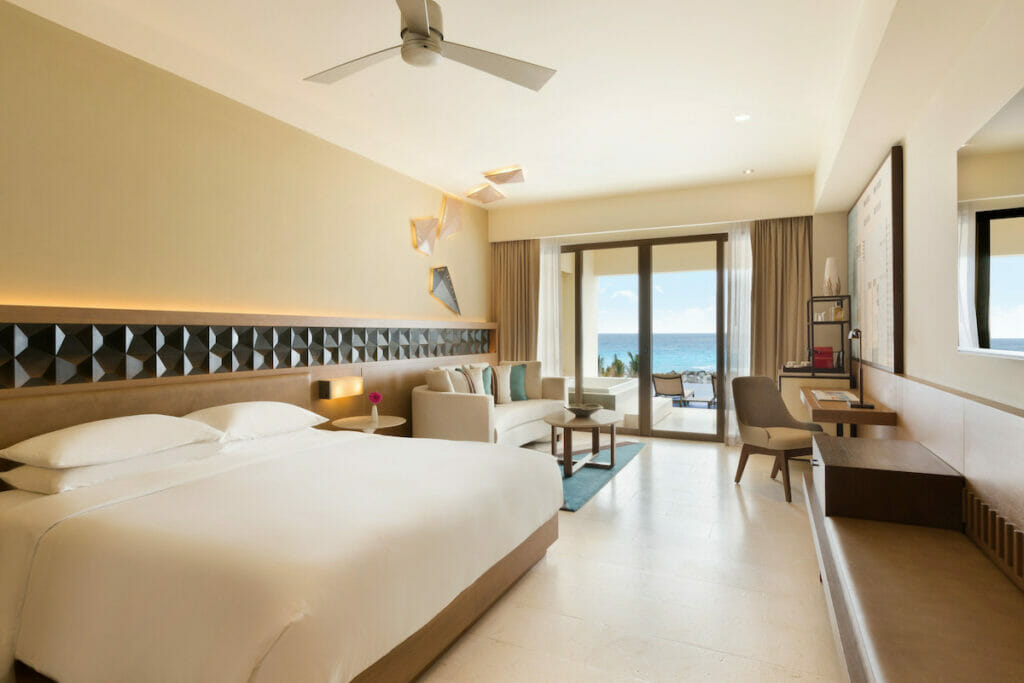Spacious room with white queen sized bed beside a white couch and a balcony with beach view of the Hyatt Ziva