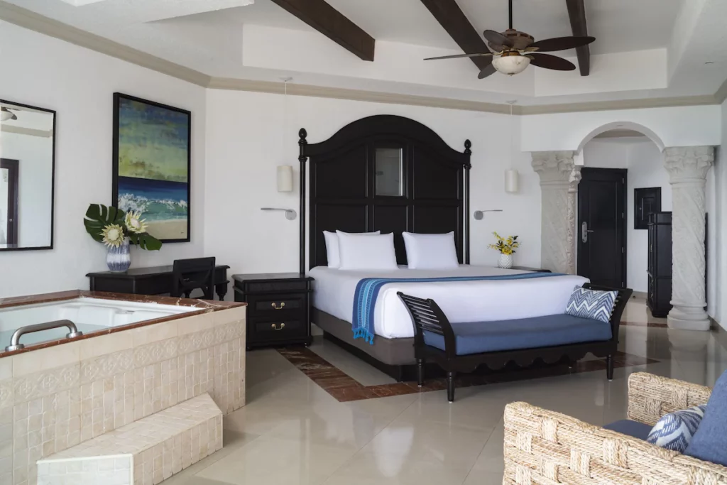 The standard room at Hyatt Zilara Cancun featuring a queen bed with a large darkwood headboard and a big bathtub on the side.