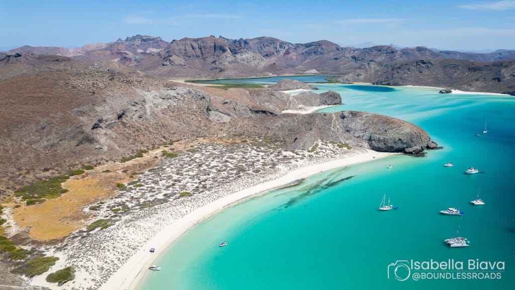 Aerial view of a stunning beach at Isla Espiritu Santo, Mexico. Turquoise waters, rocky terrain, and anchored boats create a serene landscape.