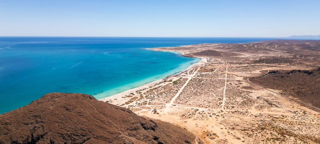Aerial view of a vast, empty beach in Baja California Sur, Mexico, with turquoise sea, arid landscape, and clear blue sky.