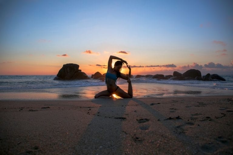 a lady doing yoga on the beach at sunset