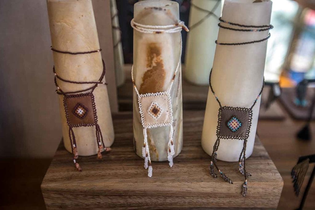 Three handwoven beaded bracelets on display, each wrapped around a cylindrical stand, showcasing detailed indigenous-style patterns in earthy tones.