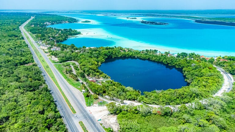 Aerial view of Laguna Bacalar's vibrant turquoise waters, lush greenery, and a road running alongside the shoreline in a serene landscape.