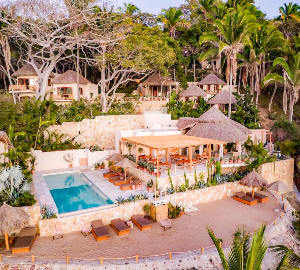 Two lounge chairs overlook a small infinity pool with panoramic views of the Pacific Ocean, framed by tropical plants and coastal hills in the distance. Tranquil, sunny setting perfect for relaxation.