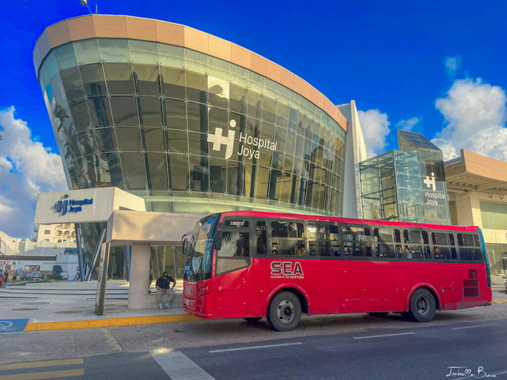 A red bus near the hospital in Cancun, Mexico under a clear sky.