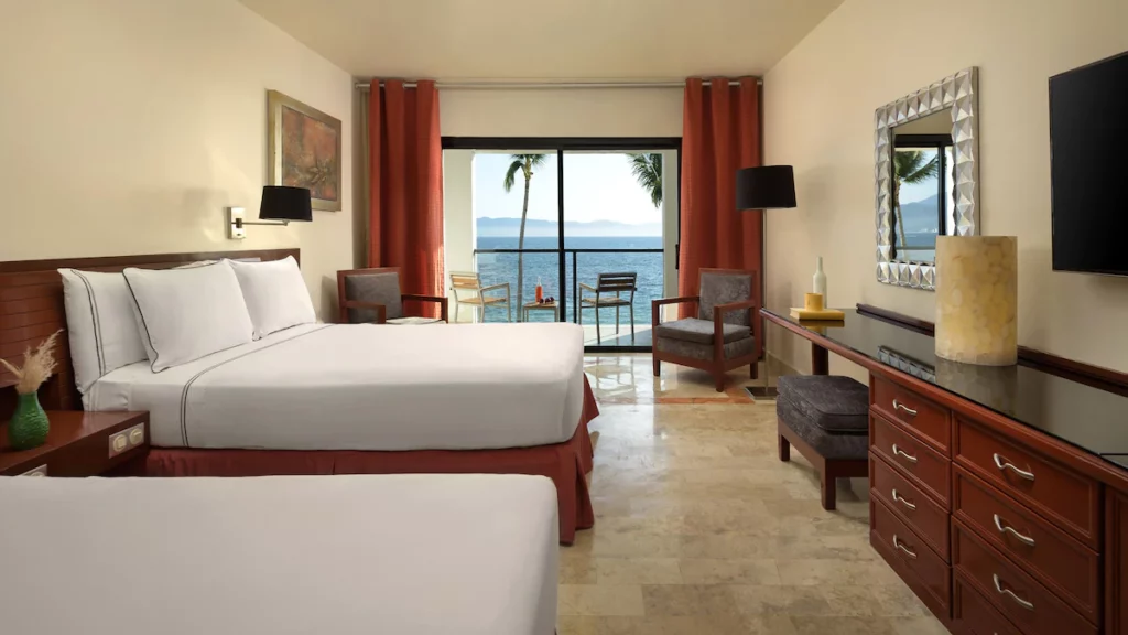 Room with a single and a queen size bed with a dark red and white color scheme and large windows with a view of the ocean.