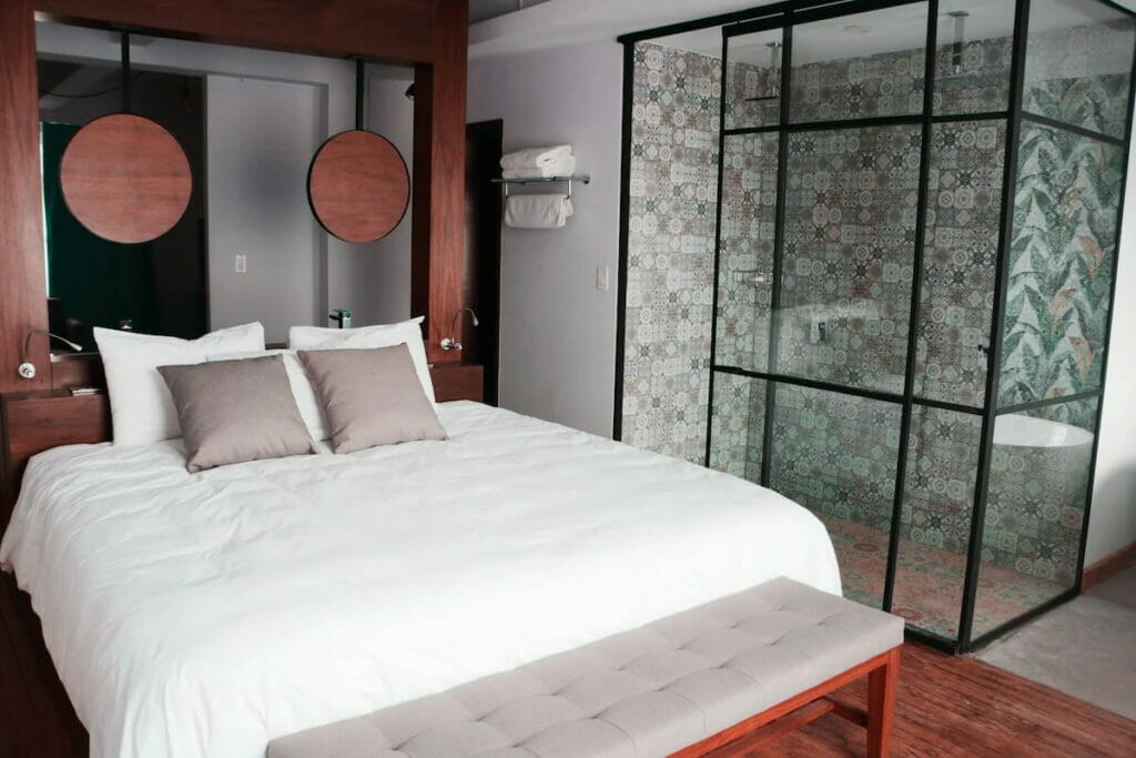 View of a bed with white sheet near the shower area - one of the boutique hotels in Mexico City.
