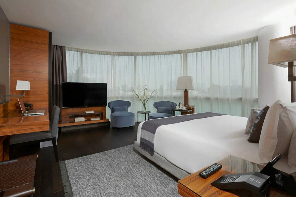 A spacious room with cozy bed, flat screen TV and multiple chairs and tables.