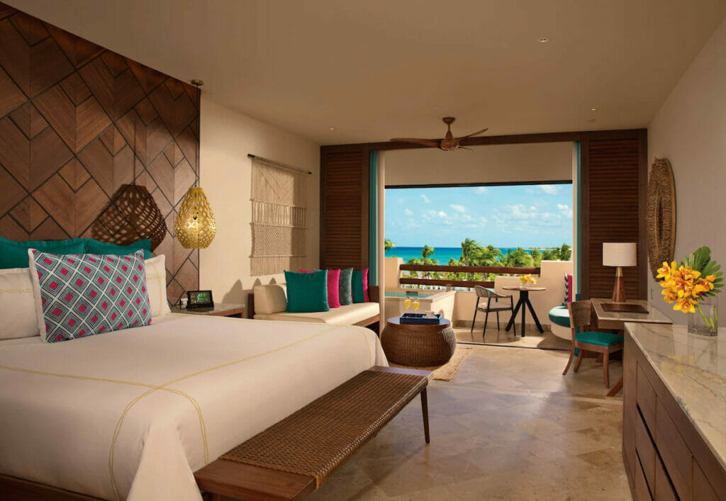 A luxury hotel in Punta Maroma with a cozy bed, tables and chairs and a balcony.