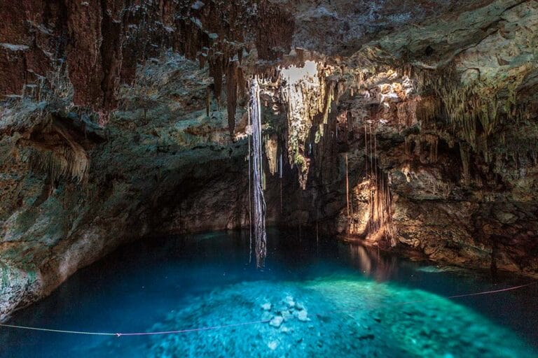 A stunning cave with blue water, illuminated by natural light. Stalactites hang from the ceiling, creating a tranquil and mysterious atmosphere.