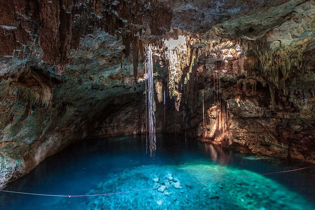 A stunning cave with blue water, illuminated by natural light. Stalactites hang from the ceiling, creating a tranquil and mysterious atmosphere.