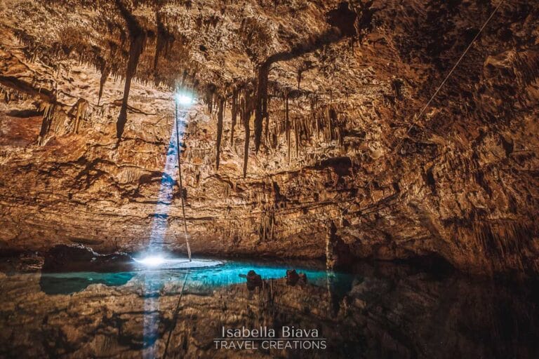 A stunning cave with stalactites and a beam of light illuminating the turquoise water below, creating a mystical atmosphere.