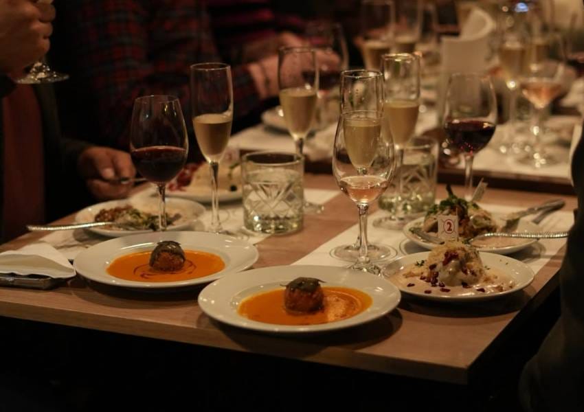 A group of people dining at a table adorned with gourmet dishes, wine glasses, and elegant tableware in a cozy restaurant setting.