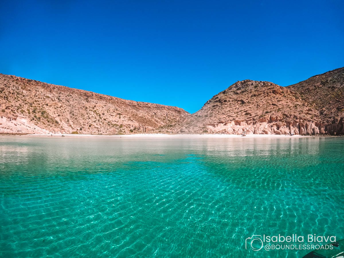 Clear turquoise waters meet a rocky shoreline under a vibrant blue sky, creating a tranquil coastal scene without any visible landmarks or people.
