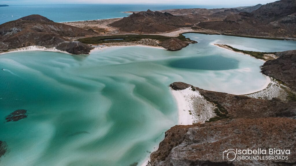 Aerial view of Balandra Beach in Baja California Sur with turquoise waters, white sand, mountainous landscape, and surrounding rugged terrain meeting the sea.