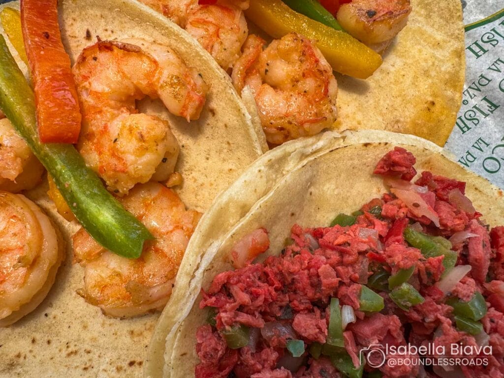 Tacos filled with seasoned shrimp, colorful bell peppers, and chopped meat. A close-up view highlights vibrant textures and ingredients.