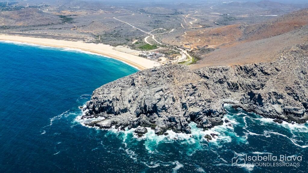 Aerial view of La Playita beach, featuring rugged cliffs, turquoise ocean waves, and desert landscape. No visible people or buildings.
