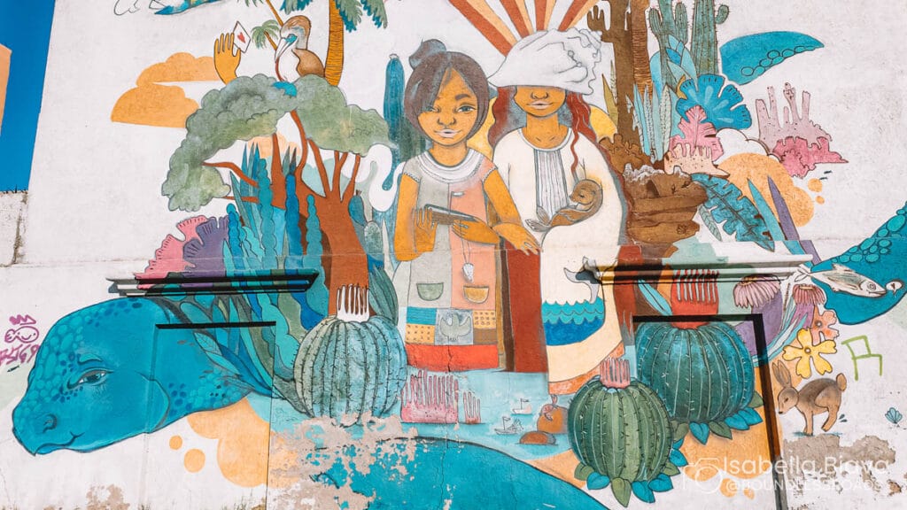 A colorful mural featuring two people surrounded by nature, animals, and cacti. The vibrant artwork embodies harmony and cultural themes.