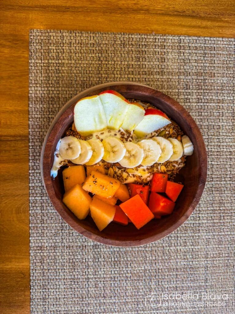 Fruit bowl with apples, bananas, and melon on mat.