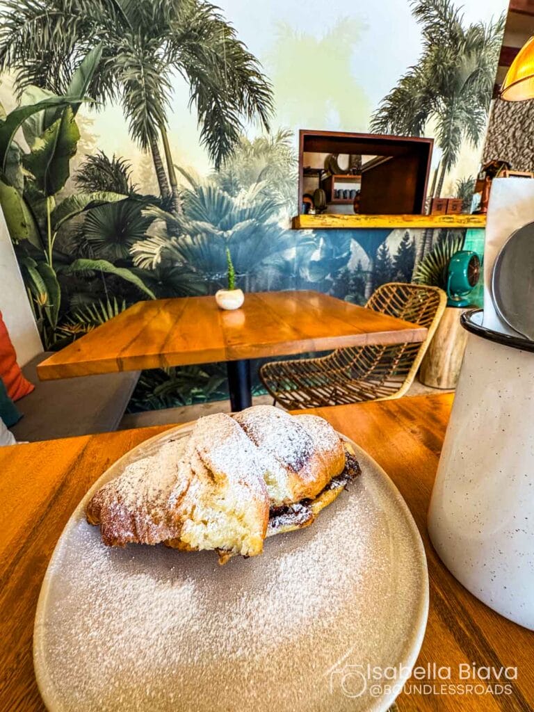 Powdered croissant on plate in tropical-themed cafe.