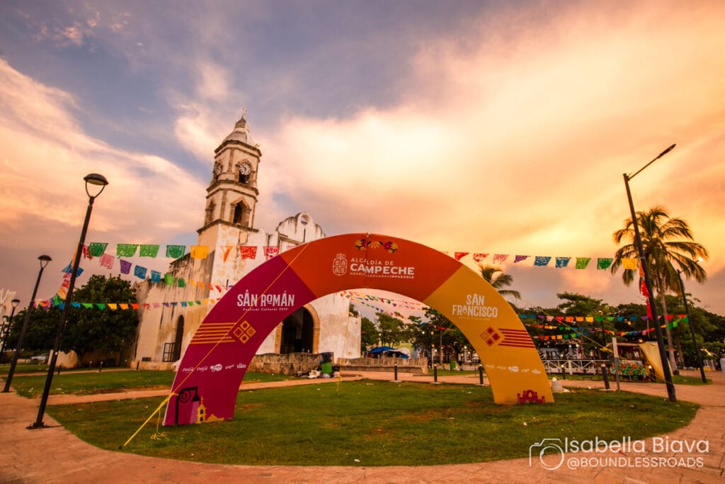 Historic festival entrance with colorful flags at sunset.