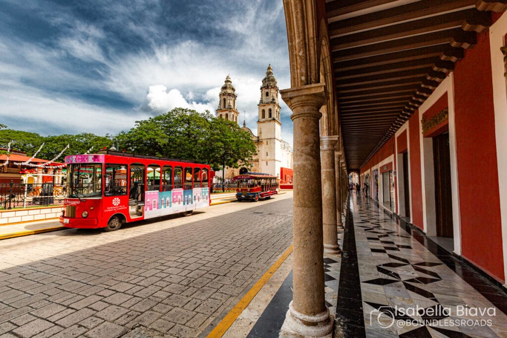Red tour bus near historic building, cloudy sky