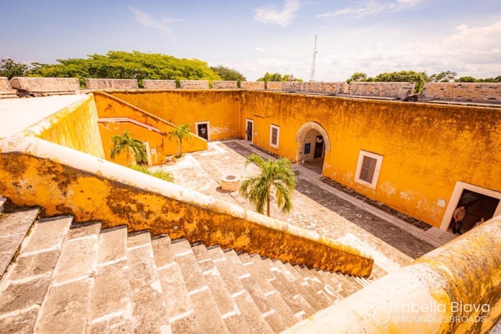 Yellow fort courtyard with stairs and palm trees.
